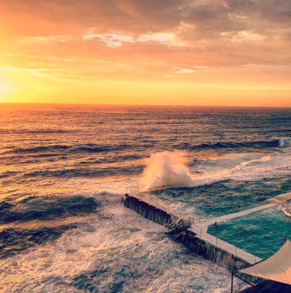 Sunrise over the ocean pool at Bondi as a wave breaks over the wall